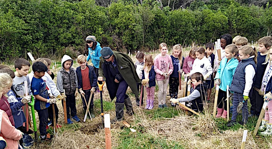 lindy demonstrating how to plant a tree as the children gathered around and watched