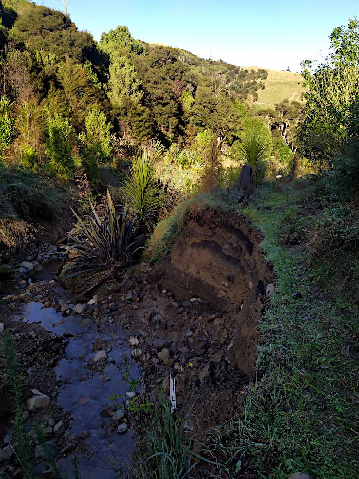 A picture showing how the edge of a track has been eaten away by the flooding of the creek